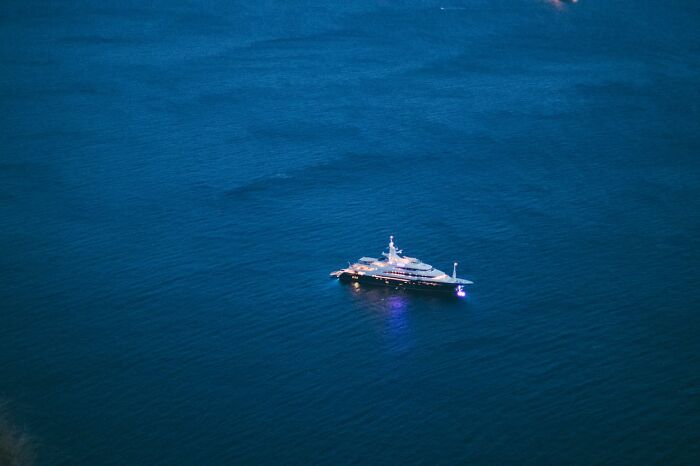 Luxury yacht illuminated at dusk on calm ocean waters, evoking very stupid very lucky terrifying moments at sea.