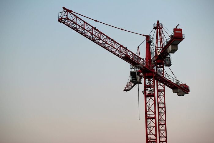 Red construction crane against clear sky, illustrating jobs related to ultra-wealthy people and luxury projects.