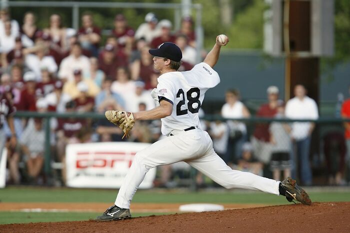 Baseball pitcher in white uniform throwing ball mid-game, illustrating people who were villains in others' stories.