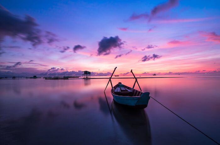 Small boat on calm water at sunset with vibrant colors, illustrating unexpected travel destinations not as pictured.
