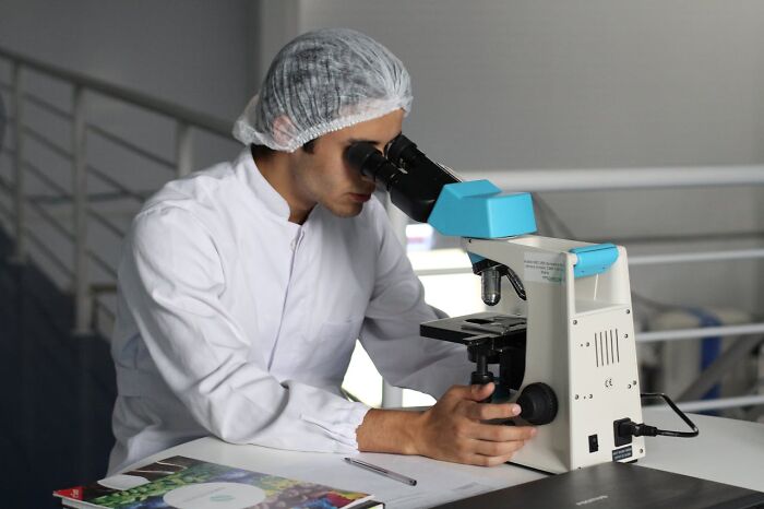 Doctor in lab coat using microscope in a clinical setting studying samples related to rare disease diagnosis and research.