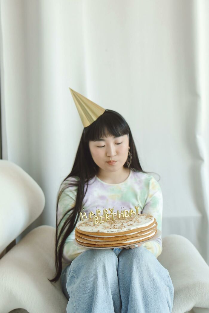 Young woman wearing a party hat holding a birthday cake, reflecting on gender role differences women are not allowed to do.