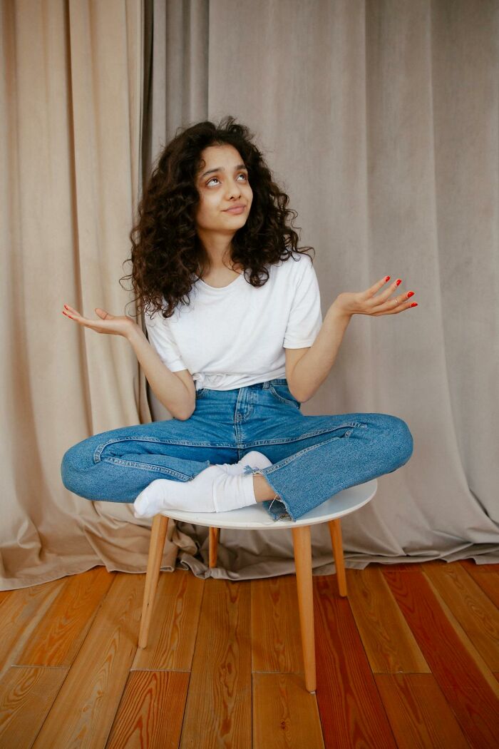 Young woman sitting cross-legged on a chair, looking puzzled, reflecting on people who were the villain in someone else’s story.