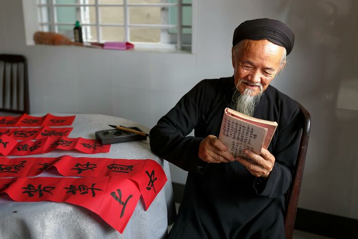 Elderly man with a sweet facade smiling gently while reading a book, hiding manipulation and betrayal in real life.