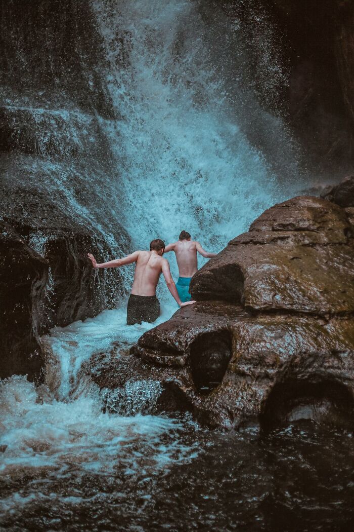 Two people in swimwear navigating a powerful waterfall, capturing a very stupid very lucky terrifying moment outdoors.