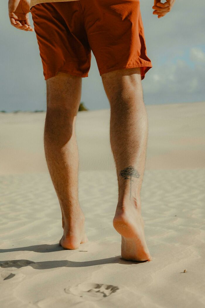 Man walking barefoot on sand wearing orange shorts, illustrating gender freedom in things women are not allowed to do.