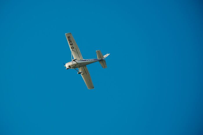 Small white airplane flying against clear blue sky, capturing a very lucky and terrifying moment in flight.