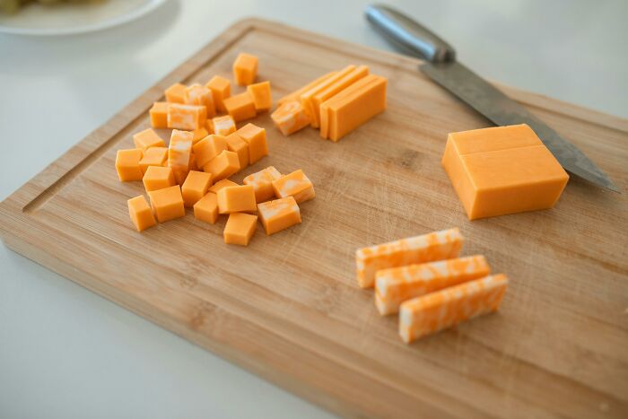 Cheese being cut into small cubes and slices on a wooden cutting board with a knife, illustrating pointless time-consuming tasks.