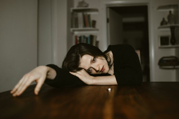 A woman in a black top lying on a wooden table, looking tired and reflective, illustrating marriage pressure effects.
