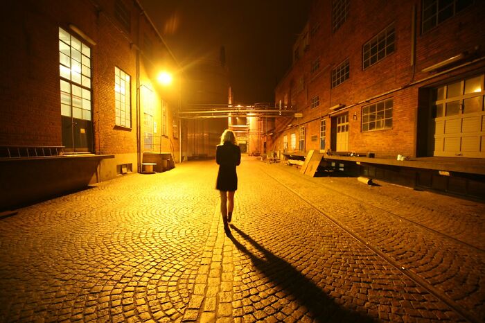 A woman walking alone in an empty industrial street at night, highlighting things women are not allowed to do.