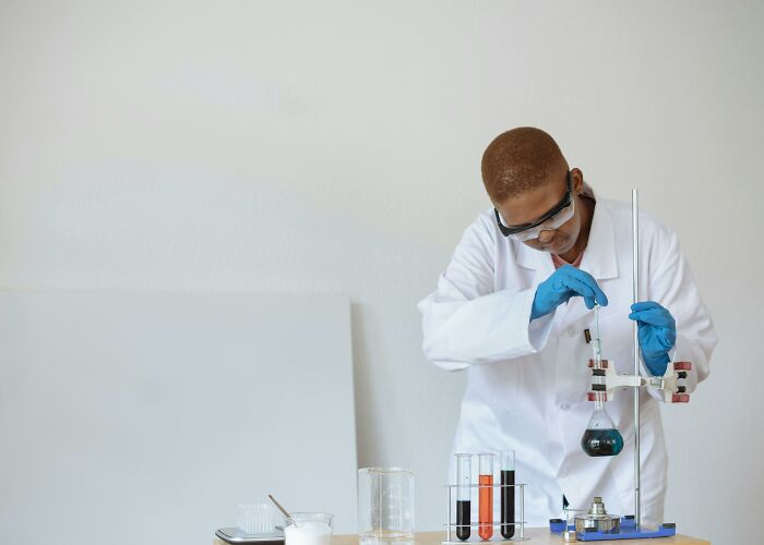 Scientist in a white lab coat and blue gloves conducting a chemistry experiment with test tubes and a flask.