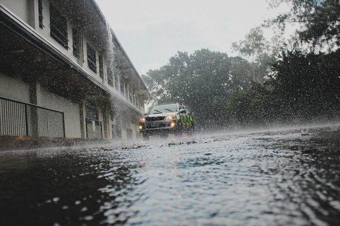 Car driving on a wet road during heavy rain with water splashing and trees in the background.