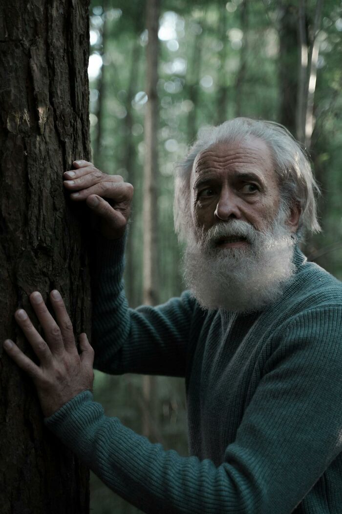Elderly man with white beard looking scared and holding a tree in the woods depicting creepy encounters while alone.