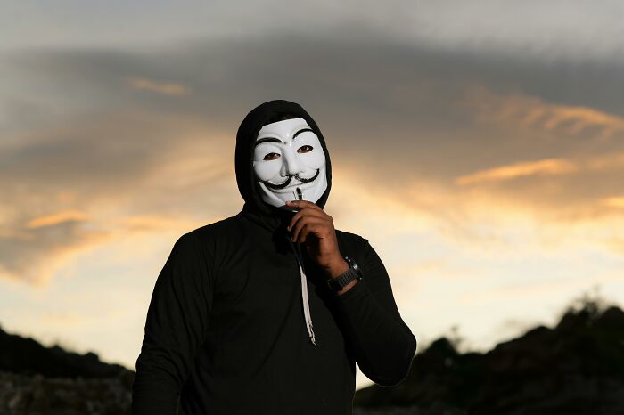 Person wearing a Guy Fawkes mask at sunset representing unexplained mysteries from the dawn of the internet.