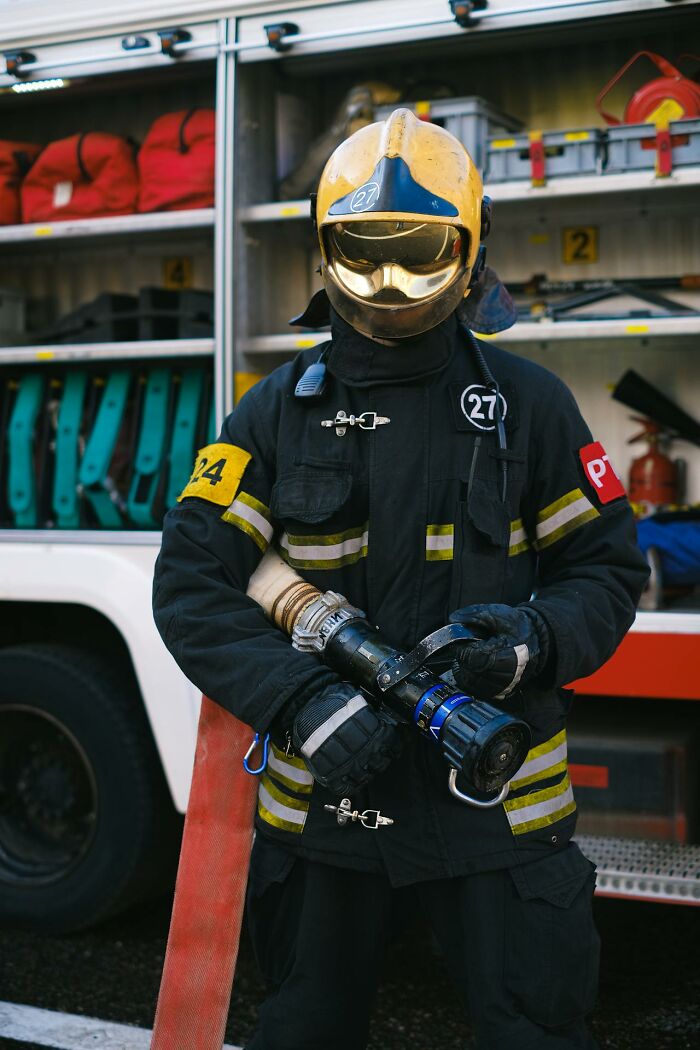 Firefighter in full gear holding a fire hose nozzle in front of a fire truck, illustrating villain impact in someone else’s story.