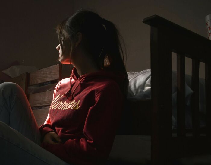 Teenage daughter sitting alone in a dark room, heartbroken as parents prefer watching TV all day than spending time with her.