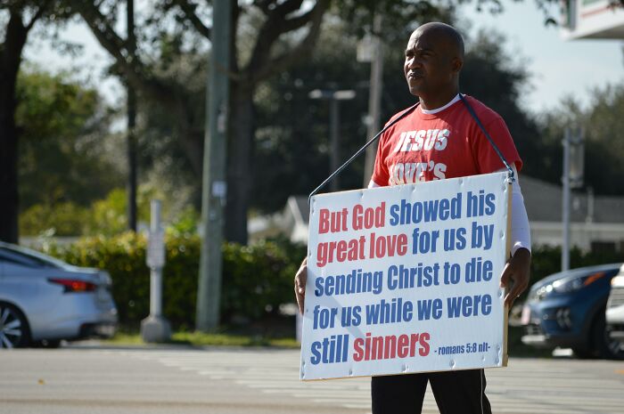 Man holding a sign with a religious message, illustrating how a sweet facade can hide manipulation or lies in real life.
