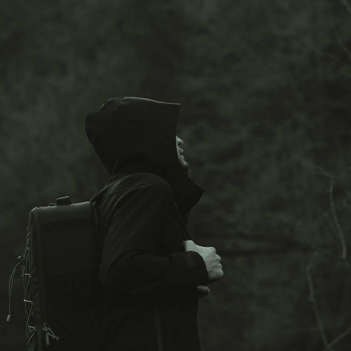 Person in a dark hooded jacket with a backpack, standing alone outside, evoking a home alone and horrifying feeling.