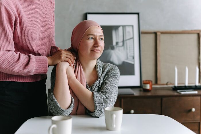 Woman wearing headscarf sitting at table with supportive person holding her arm, symbolizing patient with rare disease encounter.