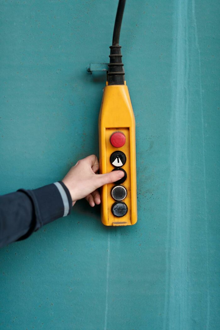Hand pressing button on yellow control panel against blue wall, illustrating careless actions leading to getting fired.