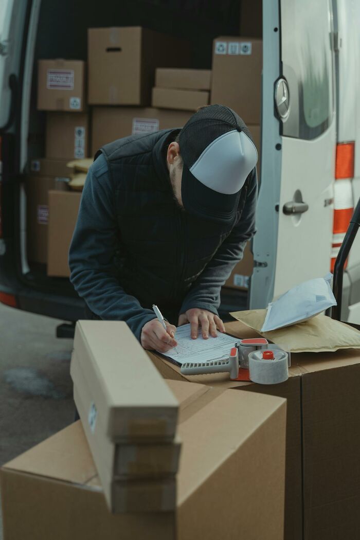 Delivery worker checking packages and signing documents amid stacked boxes, illustrating people who were the villain in stories.