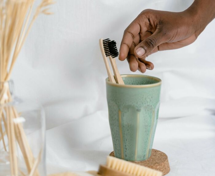 Hand placing bamboo toothbrush into a green cup illustrating nasty things exes did that shocked and grossed out partners.
