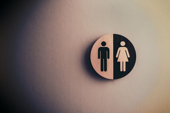 Round wooden restroom sign with male and female icons on a beige wall, related to fastest ways to get fired.