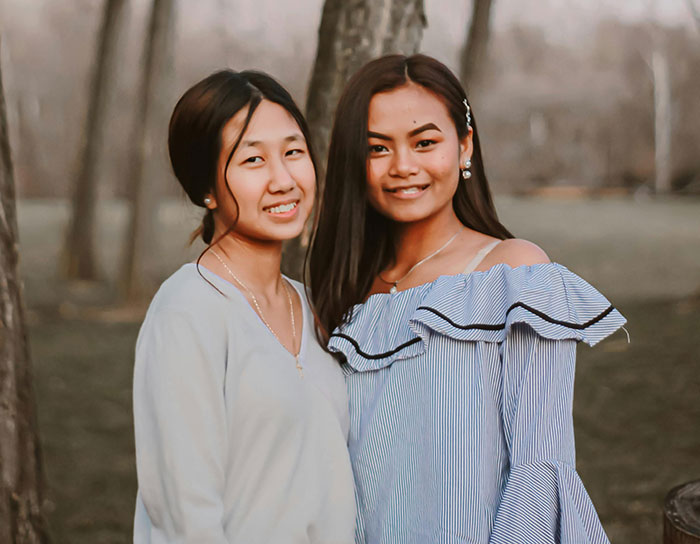 Two sisters standing outdoors near trees, smiling, representing siblings facing HOA housing dispute challenges.