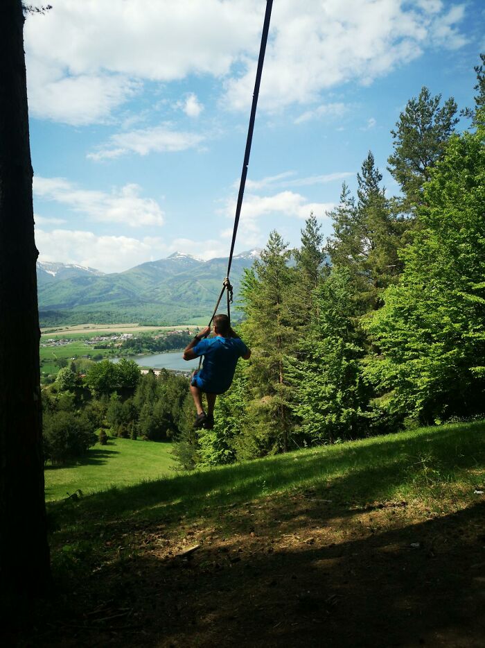 Person swinging on a rope swing over a hillside with trees and mountains, evoking moments of survival and thrill.