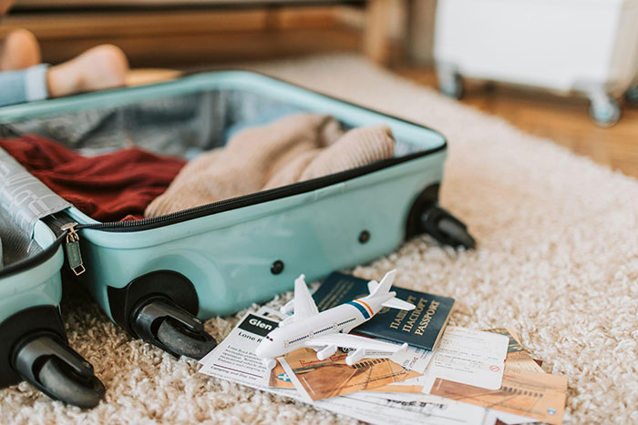 Open suitcase with clothes and toy airplane on carpet, illustrating entitled lady manipulating boyfriend and demanding free rides.