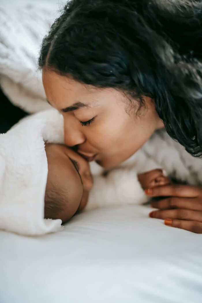 Mother gently kissing her baby wrapped in a blanket, illustrating rare disease patient care and emotional support moments.