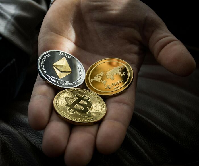 Hand holding physical cryptocurrency coins including Bitcoin, Ethereum, and Ripple representing the next big thing that totally flopped concept.