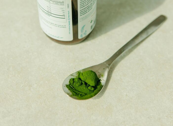 Green powder supplement on a spoon next to a bottle, representing overhyped products people say to stop buying.