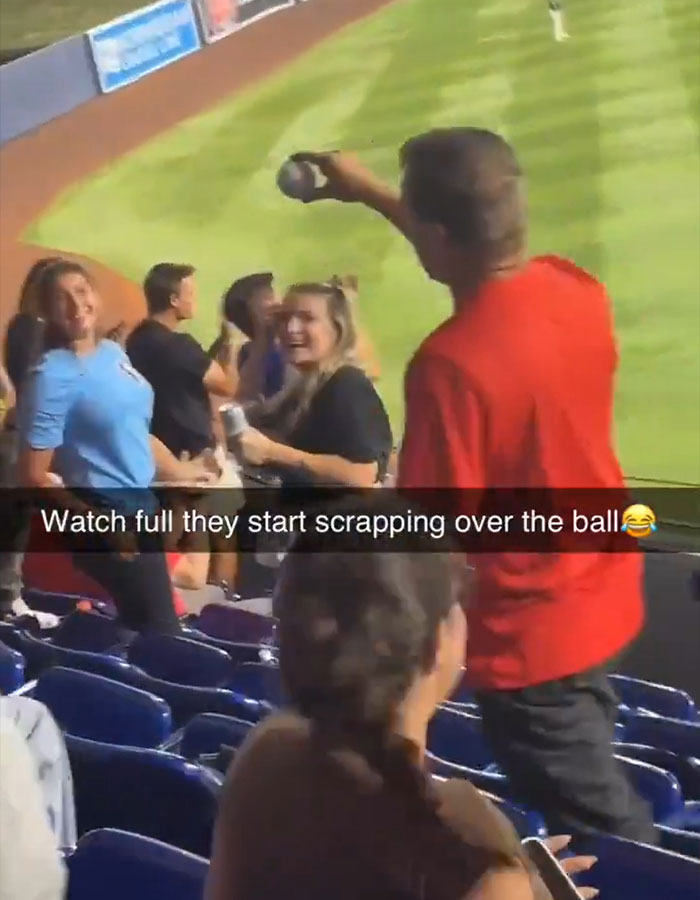 Woman in red Phillies shirt holding home run ball at stadium, causing crowd reaction during baseball game incident.