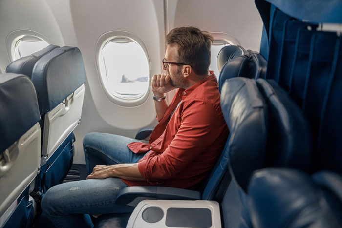 Passenger sitting in airplane seat by the window, looking outside, during a dramatic journey involving a family and seat dispute.