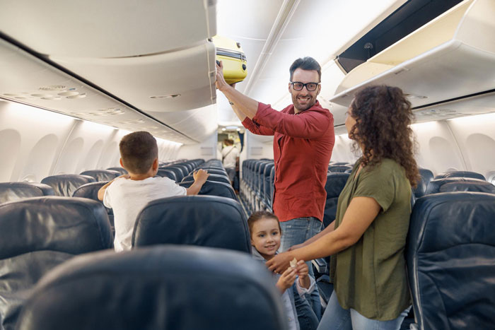 Family watches passenger placing luggage in overhead bin on airplane, creating tension during the journey.