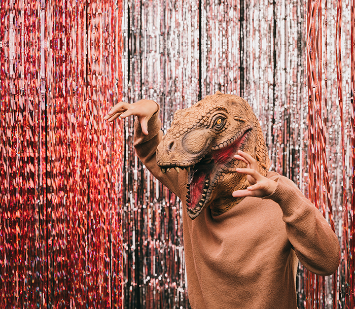 Man wearing a dinosaur mask playfully posing against metallic red and silver backdrop during a schizophrenic man prank hospital visit event