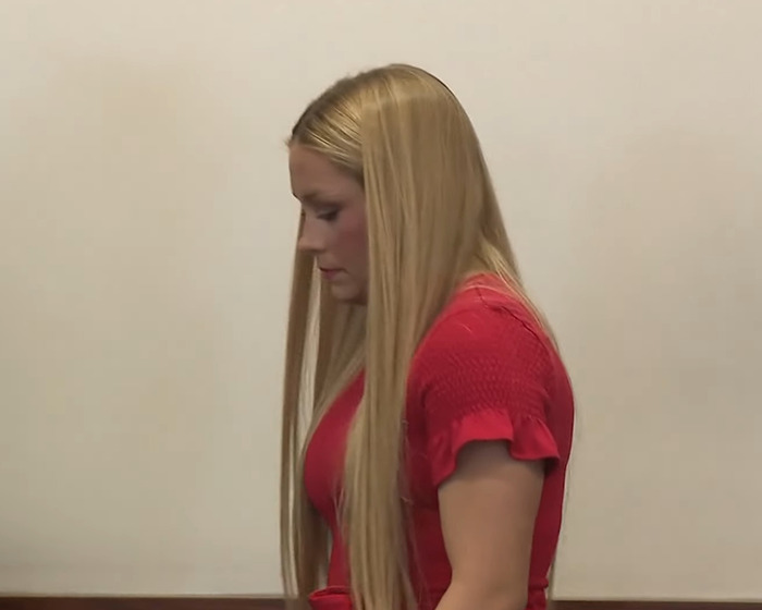 Woman with long blonde hair in a red dress standing in a courtroom setting discussing Kentucky cheerleader baby case details. Woman with long blonde hair in a red dress standing in a courtroom setting discussing Kentucky cheerleader baby case details.