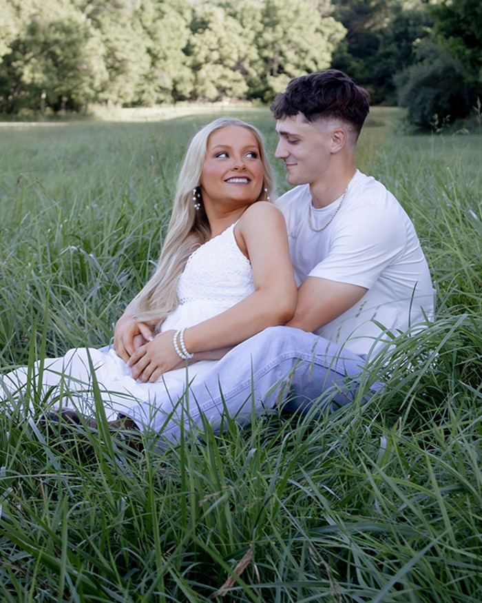 Young couple sitting in a grassy field, with the woman wearing a white dress and the man in a white shirt and jeans. Young couple sitting in a grassy field, with the woman wearing a white dress and the man in a white shirt and jeans.