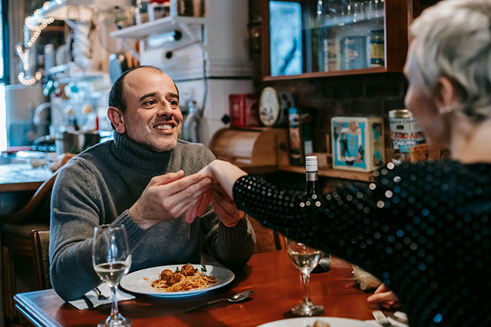 Man in a cozy restaurant holding a woman&rsquo;s hand, illustrating themes of polyamory and open marriage.