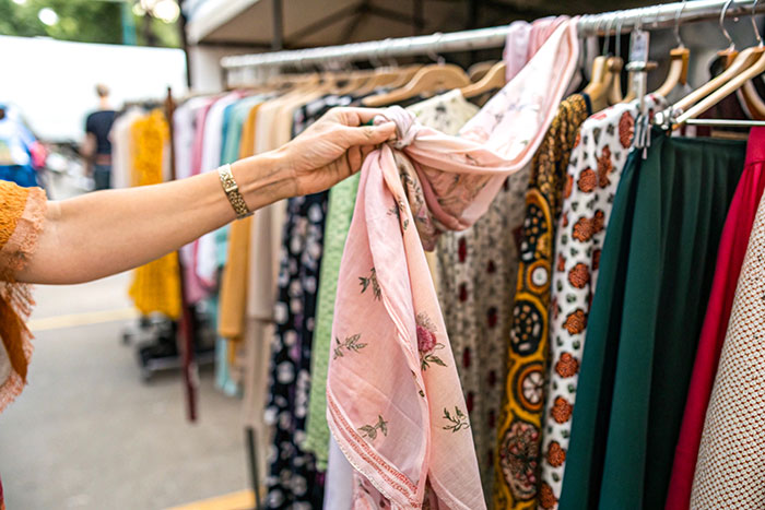 Person holding a pink scarf while browsing various clothes on a rack, illustrating habits people who used to be poor have.
