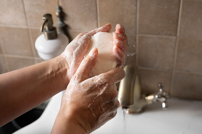 Person washing hands with soap at a sink, illustrating habits people who used to be poor can't get rid of.
