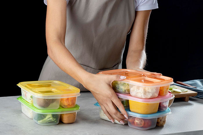 Person packing multiple containers with food, illustrating habits people who used to be poor can’t get rid of.