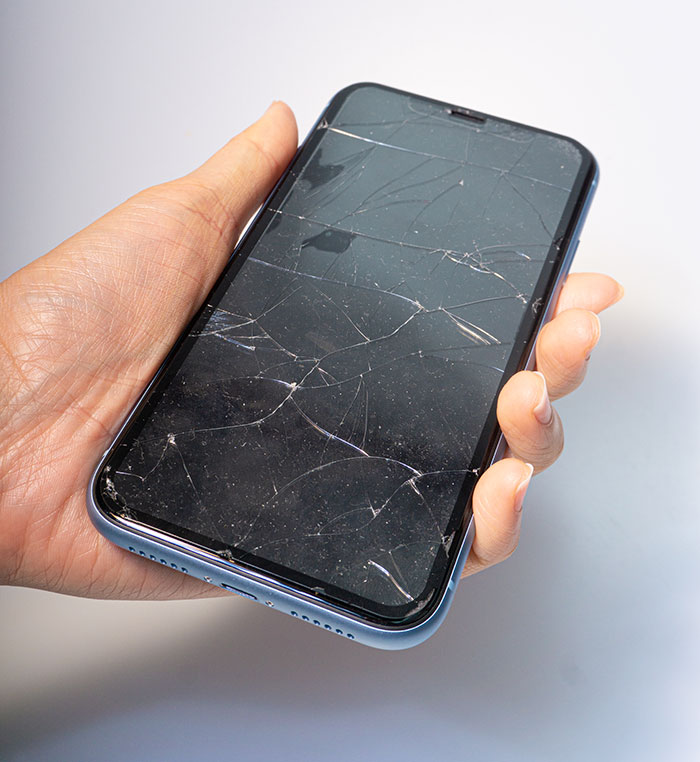 Hand holding a c*****d smartphone screen, illustrating common habits people who used to be poor can't get rid of.