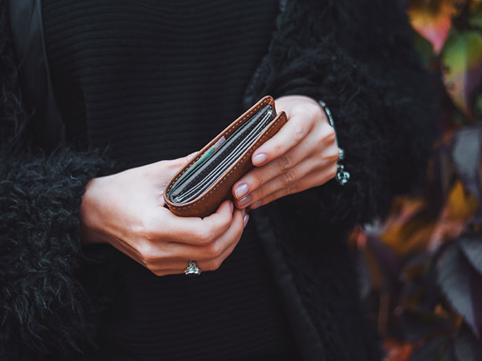 Person holding a brown wallet outdoors, illustrating habits people who used to be poor can't get rid of related to money management.
