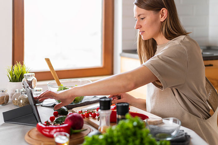 Woman preparing fresh vegetables in a kitchen while using a tablet, illustrating habits people who used to be poor can't get rid of.