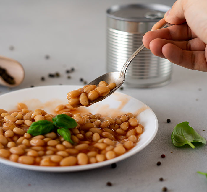 Hand holding spoon with beans from a plate, illustrating habits people who used to be poor can't get rid of.