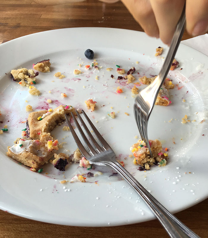 A person scraping crumbs from a plate with fork, illustrating habits people who used to be poor can't get rid of.
