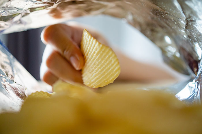 Hand reaching into a bag of potato chips illustrating habits people who used to be poor can't get rid of.