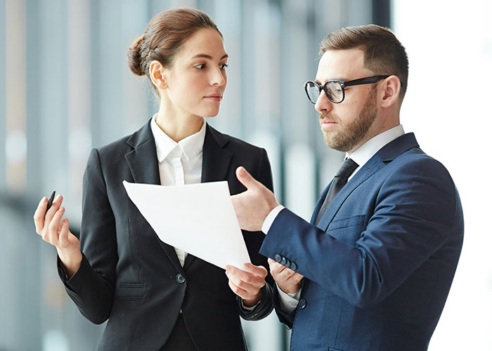 Two professionals in business attire discussing documents, illustrating job descriptions that are technically true.